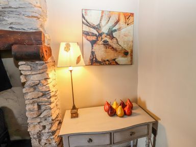 A table with a lamp and decorative pears under a painting of a deer next to a stone wall at Low Cartmell Fold in Crosthwaite