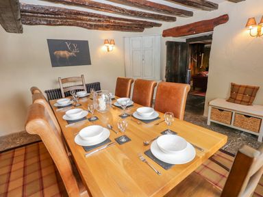 A dining room with a wooden table set for six with bowls glasses and cutlery with leather chairs and wooden beams on the ceiling at Low Cartmell Fold in Crosthwaite