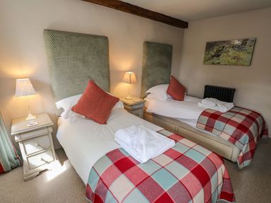A bedroom with two single beds side by side each with a red plaid blanket and an orange pillow at Low Cartmell Fold in Crosthwaite