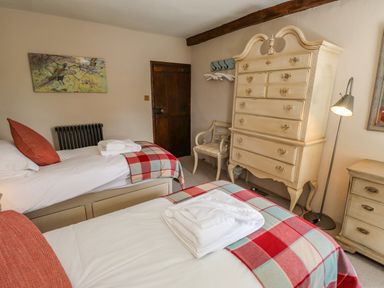 A bedroom with two single beds with checkered blankets a chest of drawers wooden door and a chair at Low Cartmell Fold in Crosthwaite
