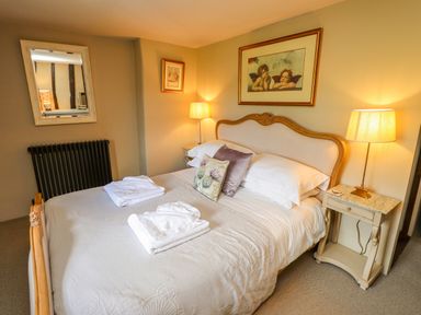 A bedroom with a double bed bedside tables lamps a mirror and framed pictures at Low Cartmell Fold in Crosthwaite