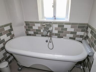 A bathroom with a white clawfoot bathtub under a window and tiled walls at Low Cartmell Fold in Crosthwaite