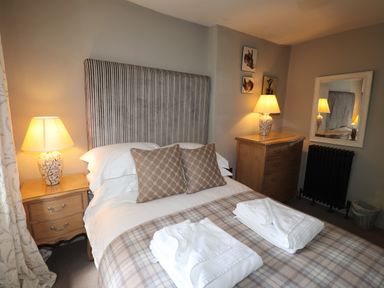 A bedroom with a double bed with striped headboard bedside tables with lamps a wooden chest of drawers and a mirror at Low Cartmell Fold in Crosthwaite