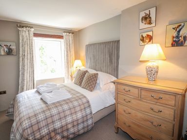 A bedroom with a bed with folded towels bedside tables lamps and a chest of drawers with animal paintings on the walls at Low Cartmell Fold in Crosthwaite
