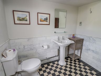 A bathroom with a toilet, pedestal sink, small cabinet, mirror, and two framed pictures on the wall at Low Cartmell Fold in Crosthwaite