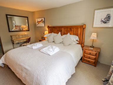 A bedroom with a large wooden bed with white bedding and pillows beside wooden nightstands with lamps at Low Cartmell Fold in Crosthwaite