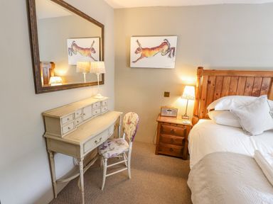 A bedroom with a wooden bed white bedding a vintage desk with a floral chair a large mirror and a painting of a running hare at Low Cartmell Fold in Crosthwaite