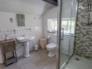A bathroom with a pedestal sink a toilet a shower with glass doors and tiled walls a small cabinet and a laundry basket at Low Cartmell Fold in Crosthwaite