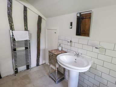 A bathroom with a pedestal sink a small cabinet a heated towel rail and wooden beams on the wall at Low Cartmell Fold in Crosthwaite