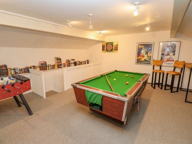 A game room with a pool table foosball table dartboard bookshelves and bar stools at Low Cartmell Fold in Crosthwaite
