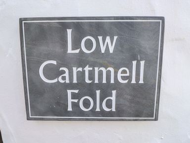 A square stone sign with the words Low Cartmell Fold mounted on a white wall at Low Cartmell Fold in Crosthwaite