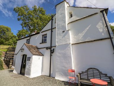 Exterior of a white building with a small porch with a door and sign Low Cartmell Fold with outdoor chairs and a bench at Low Cartmell Fold in Crosthwaite