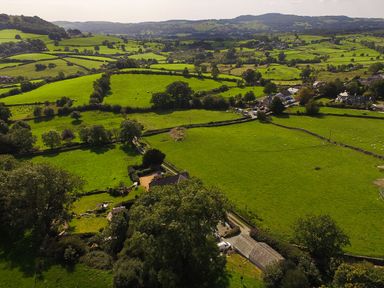 An aerial view of green fields separated by stone walls with scattered trees and houses in a rural landscape at Low Cartmell Fold in Crosthwaite