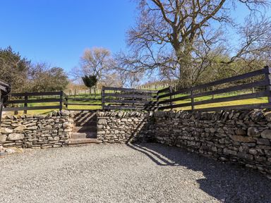 A stone wall and gravel area with steps leading to a fenced grassy area and trees at Low Cartmell Fold in Crosthwaite