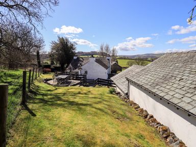 A garden area with outdoor furniture tables and chairs next to white houses with slate roofs at Low Cartmell Fold in Crosthwaite