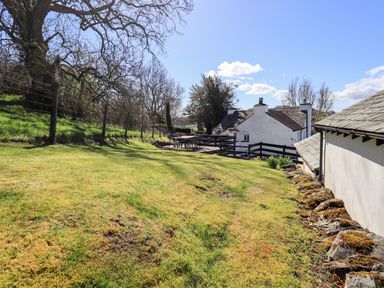 A grassy backyard with a wooden fence tables and chairs near two white houses at Low Cartmell Fold in Crosthwaite