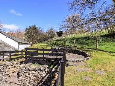An outdoor stone patio with a metal table and chairs near a grassy hillside at Low Cartmell Fold in Crosthwaite