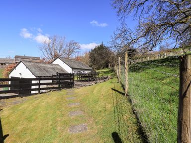A grassy outdoor area with stone steps a metal fence and black chairs and tables near white buildings at Low Cartmell Fold in Crosthwaite