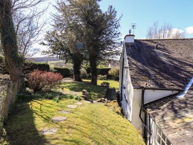A garden with a stone path trees bushes and part of a house roof at Low Cartmell Fold in Crosthwaite