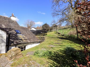 A grassy path beside a white cottage with a stone roof and a wooden fence at Low Cartmell Fold in Crosthwaite
