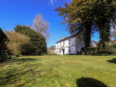 A large lawn with bushes and trees surrounding a white house at Low Cartmell Fold in Crosthwaite