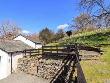An outdoor stone terrace with a table and chairs surrounded by a stone wall and wooden fence at Low Cartmell Fold in Crosthwaite