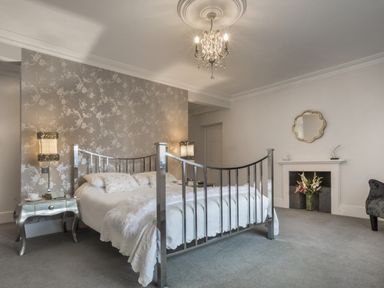 A bedroom with a metal bed frame bedside tables lamps wallpaper and a fireplace with flowers at Tent Lodge in Coniston