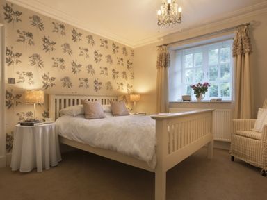 A bedroom with a bed lamps a chair and a window with flowers on the windowsill at Tent Lodge in Coniston