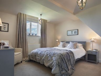 A bedroom with a bed covered in a fur throw and pillows two bedside tables with lamps and a window with curtains at Tent Lodge Coniston
