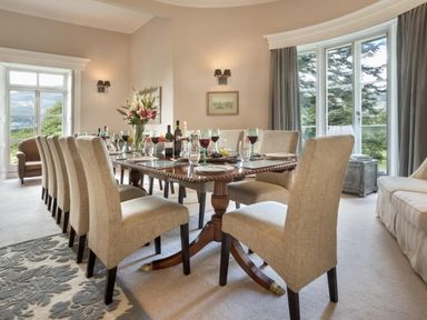 A dining room with a wooden table and beige chairs near large windows at Tent Lodge in Coniston