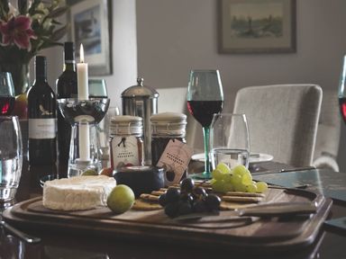 A dining table with cheese, grapes, preserves, wine bottles, glasses and a lit candle at Tent Lodge in Coniston