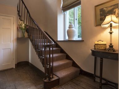 An interior stairway with wooden banister carpeted steps a small table with a lamp and decorative box a window with a ceramic vase and flowers in a vase Tent Lodge Coniston