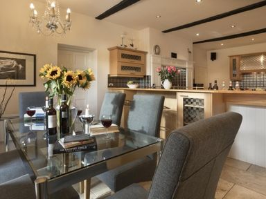 A dining area with a glass table and gray chairs sunflowers in a vase wine glasses and bottles in a kitchen at Tent Lodge in Coniston