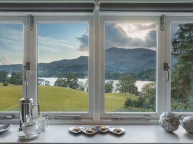 A window view showing green hills lake and mountains with a coffee set and candles on the windowsill at Tent Lodge in Coniston
