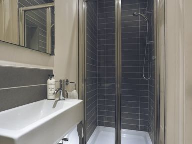 A bathroom with a white rectangular sink a bottle of soap a towel ring and a glass shower enclosure with dark tiles at Tent Lodge in Coniston