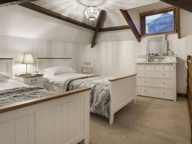 A bedroom with two single beds bedside table lamp and a dresser with mirror at Tent Lodge in Coniston