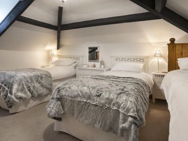 A bedroom with three single beds and bedside tables under a ceiling with dark wooden beams at Tent Lodge in Coniston