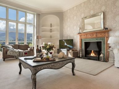 A living room with a fireplace a patterned coffee table and large windows at Tent Lodge in Coniston