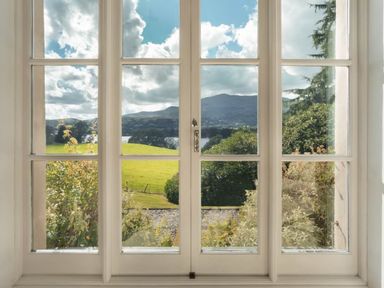 A window with glass panes showing a view of green fields bushes trees and mountains under a partly cloudy sky at Tent Lodge in Coniston