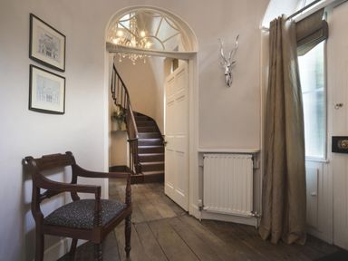A hallway with a wooden floor chair radiator and staircase at Tent Lodge in Coniston