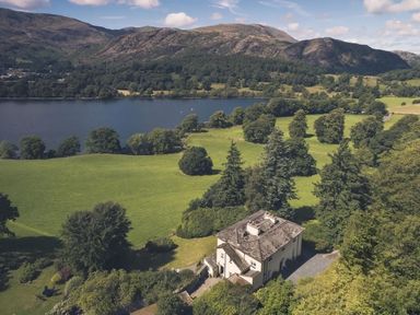 A house surrounded by trees and fields near a lake with hills in the background at Tent Lodge in Coniston