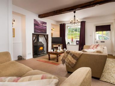 A living room with beige sofas a wood burning stove and a window with curtains at Pollys Cottage in Langdale