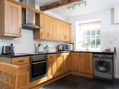 A kitchen with wooden cabinets a washing machine an oven a microwave and a window at Pollys Cottage in Langdale
