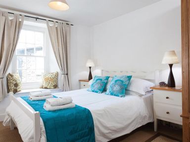 A bedroom with a double bed two turquoise pillows folded towels bedside tables and window seats at Pollys Cottage in Langdale