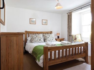 A bedroom with a wooden bed frame a green throw pillows on a window seat and wooden furniture at Pollys Cottage in Langdale