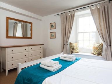 A bedroom with a bed and folded towels on it a dresser with a mirror and a window seat with cushions at Pollys Cottage in Langdale