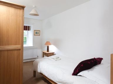 A bedroom with a single bed a wooden wardrobe bedside table with a lamp and a window at Pollys Cottage in Langdale