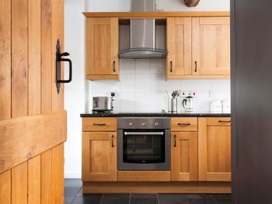 A kitchen with wooden cabinets a stainless steel oven and a tiled backsplash at Pollys Cottage in Langdale