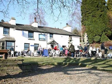 A group of people sitting and standing outside a white building with tables and chairs at Pollys Cottage in Langdale