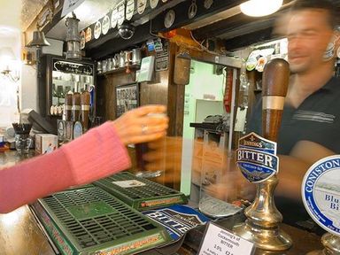 A hand reaching for a pint of beer being served by a bartender at a pub bar at Pollys Cottage in Langdale